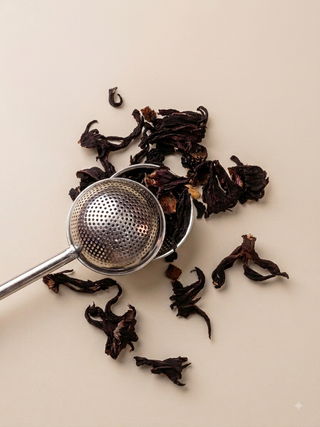 Dried dark brown hibiscus flowers with a small metal strainer spoon on a light beige background.